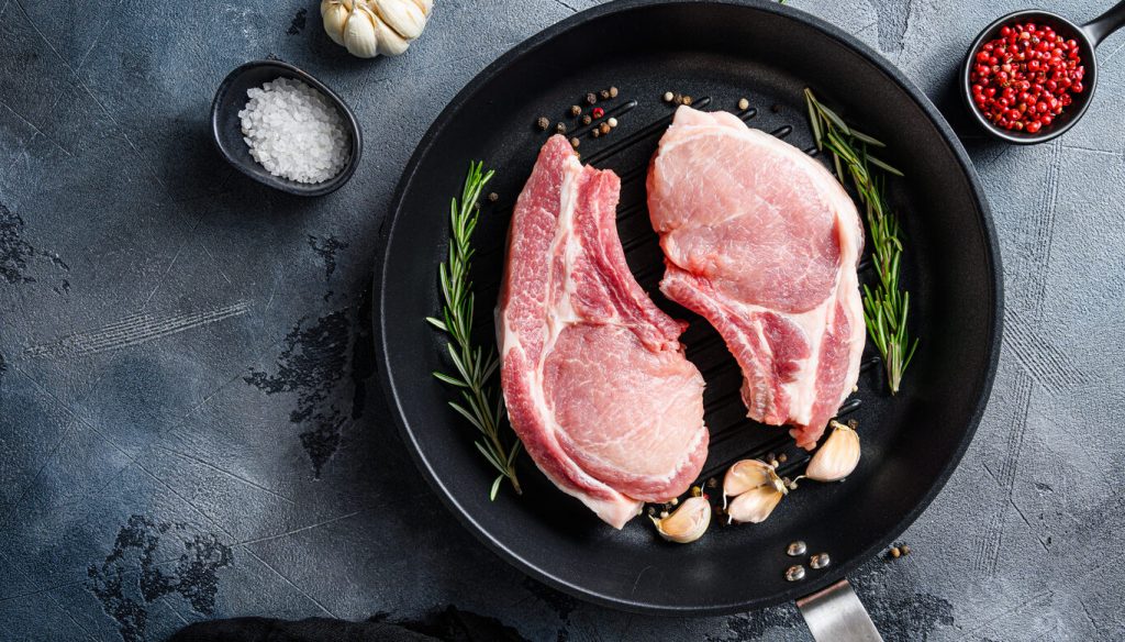 Prepared pork fillets in a skillet with herbs and spices.