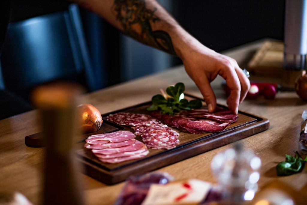 A hand arranging sliced smallgoods on a wooden serving board.